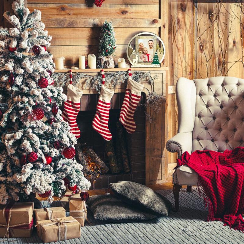 ibi100112-6-97c Navidad acogedora con árbol decorado, calcetines a rayas, regalos envueltos y sillón tufted en sala rústica.
