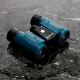 Binoculares Olympus de 8x21, impermeables, con diseño compacto y lentes antideslumbrantes sobre fondo de mármol húmedo.