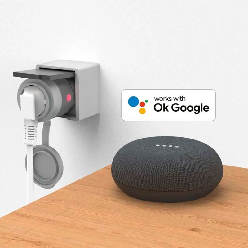 ham600001-3-04c Aura de Google en color negro, compatible con asistentes inteligentes, sobre una mesa, con enchufe visible en la pared.
