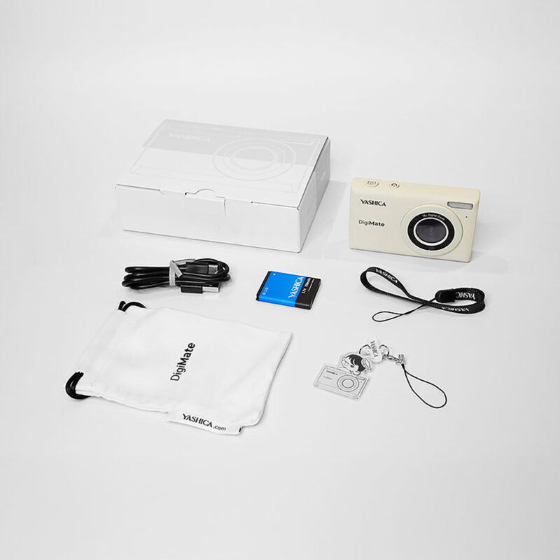yas100005-6-24d Cámara Yashica DigiMate en color crema, incluye batería, cable, estuche y llavero de cámara. Ideal para fotos casuales.