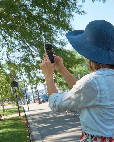 Mujer Con Sombrero Azul Usando Un Smartphone Para Tomar Fotos En Un Parque, Capturando Escenas Al Aire Libre.