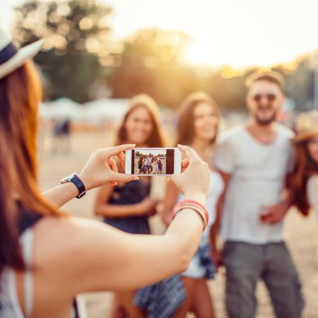 Mujer Usando Iphone 15 Pro Para Tomar Una Selfie En Un Festival Con Amigos Al Atardecer. Captura De Momentos Memorables.