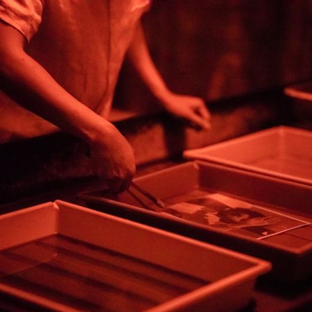 Persona Revelando Una Imagen En Un Cuarto Oscuro, Con Cubetas Y Luz Roja, Técnica De Revelado Fotográfico.