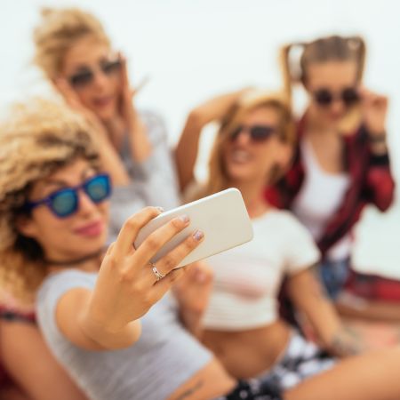 Grupo De Amigas Tomando Un Selfie Con Un Smartphone, Luciendo Gafas De Sol En Un Ambiente Relajado.