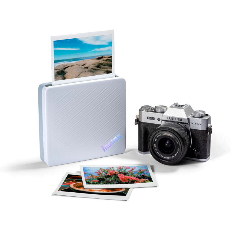 fuj170516-11-98e Cámara Fujifilm X-T30 junto a impresora Instax, con fotos impresas de paisajes y flores en primer plano.