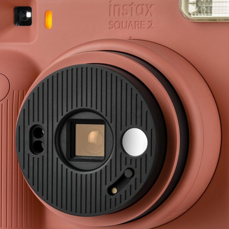 fuj170531-4-357 Cámara Instax Square 2 en color rosa, detalle del lente y visor para fotos instantáneas.
