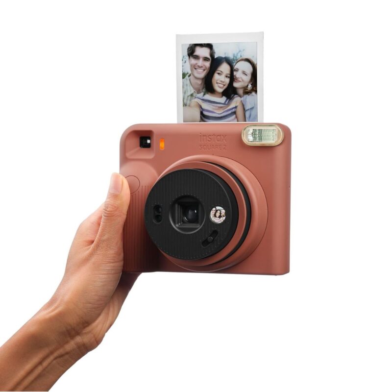 fuj170531-5-e93 Cámara instantánea Fujifilm instax SQUARE 2 en color rosa con fotografía impresa saliendo del dispositivo.